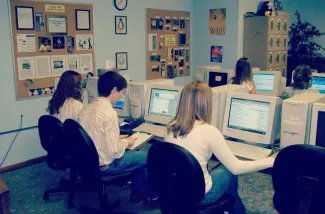 A group of people in an office using beige computers and CRT monitors